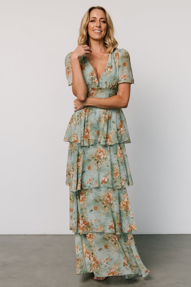 a woman in a floral print dress with her arms crossed, smiling and looking at the camera