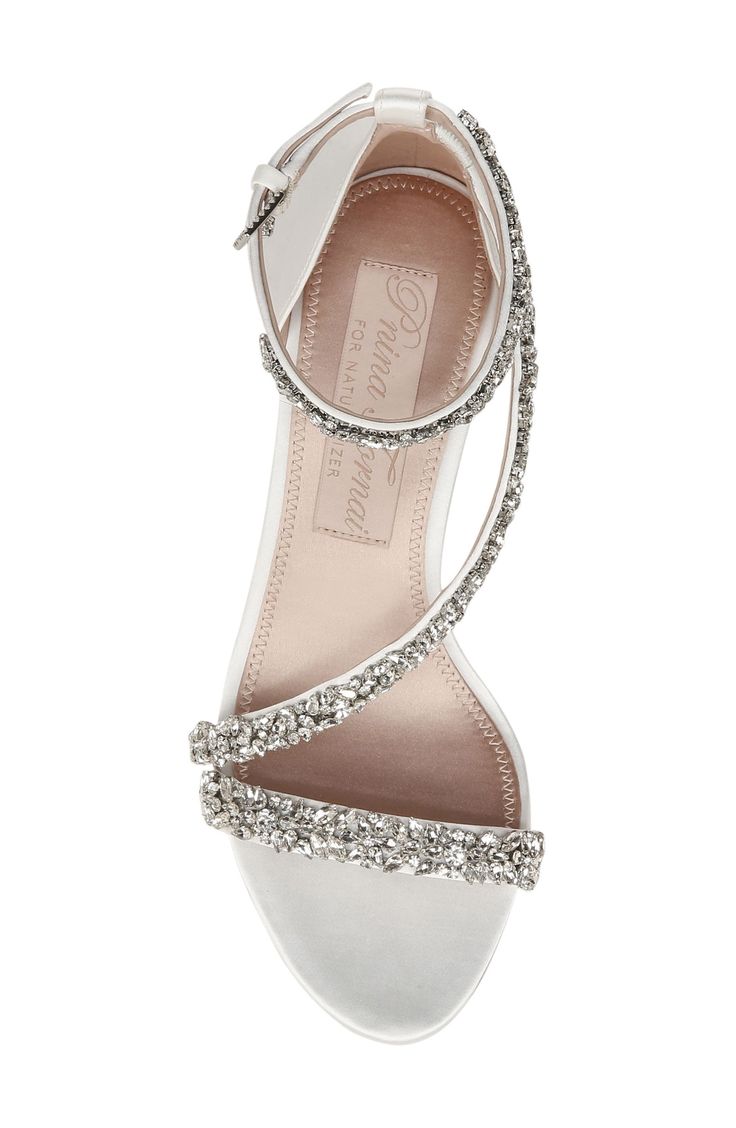 The sandal features dazzling jewels that detail slender satin straps with a wrapped block heel at the base. World-renowned bridal designer Pnina Tornai created a dreamy collection with Naturalizer of wedding-ready styles that exude luxurious elegance and are aptly named 'love' in different languages. 2 1/4" heel Cushioned footbed with Contour+ technology Slip-resistant sole Textile upper and lining/leather sole Imported Luxury Open Heel Wedding Sandals, Silver Open Toe Heels For Reception, High Heel Sandals For Reception, Bedazzled High Heel Sandals For Weddings, Silver Sandals With Heel Strap For Wedding, Block Heel Embellished Wedding Sandals, Elegant High Heel Sandals For Reception, Embellished Block Heel Wedding Sandals, Luxury Wedding Sandals With Heel Strap