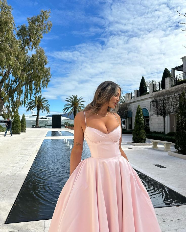 a woman standing in front of a pool wearing a pink ball gown with spaghetti straps