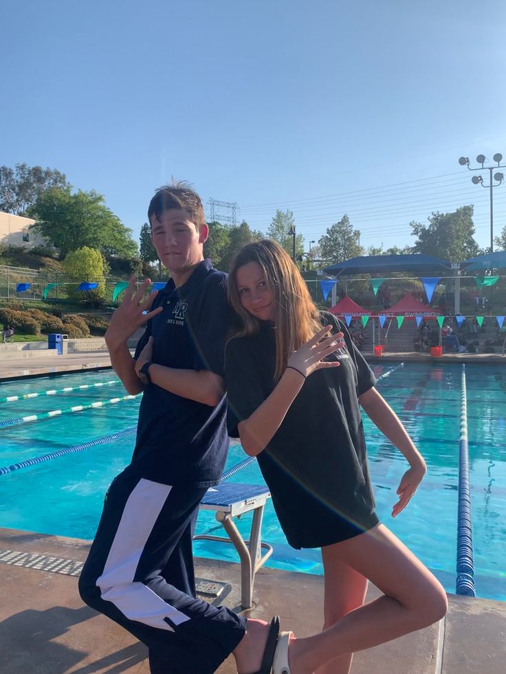 two people standing next to each other in front of a swimming pool