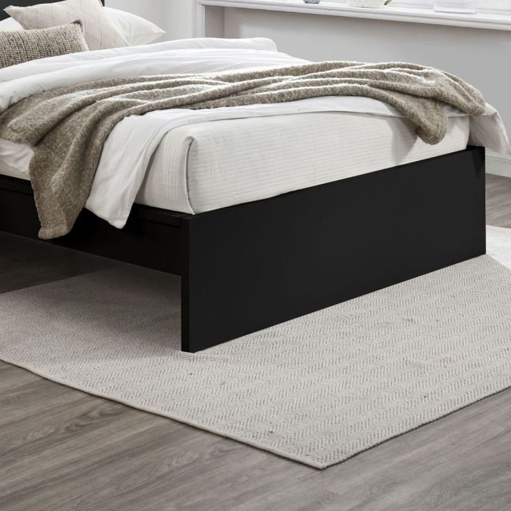 a bed sitting on top of a wooden floor next to a white and gray rug