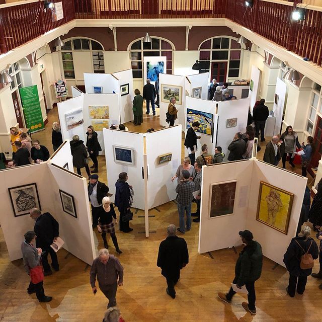 a group of people standing around looking at art on display in an open area with wooden floors