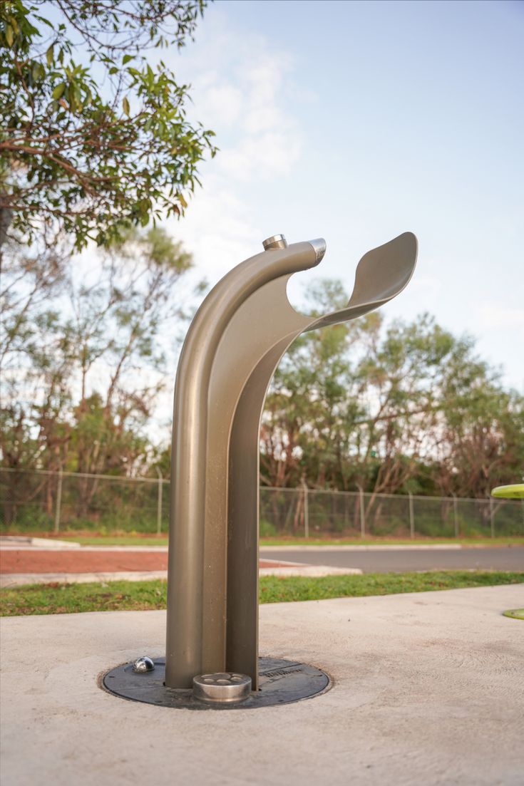 a metal sculpture in the middle of a cement area with trees and grass behind it