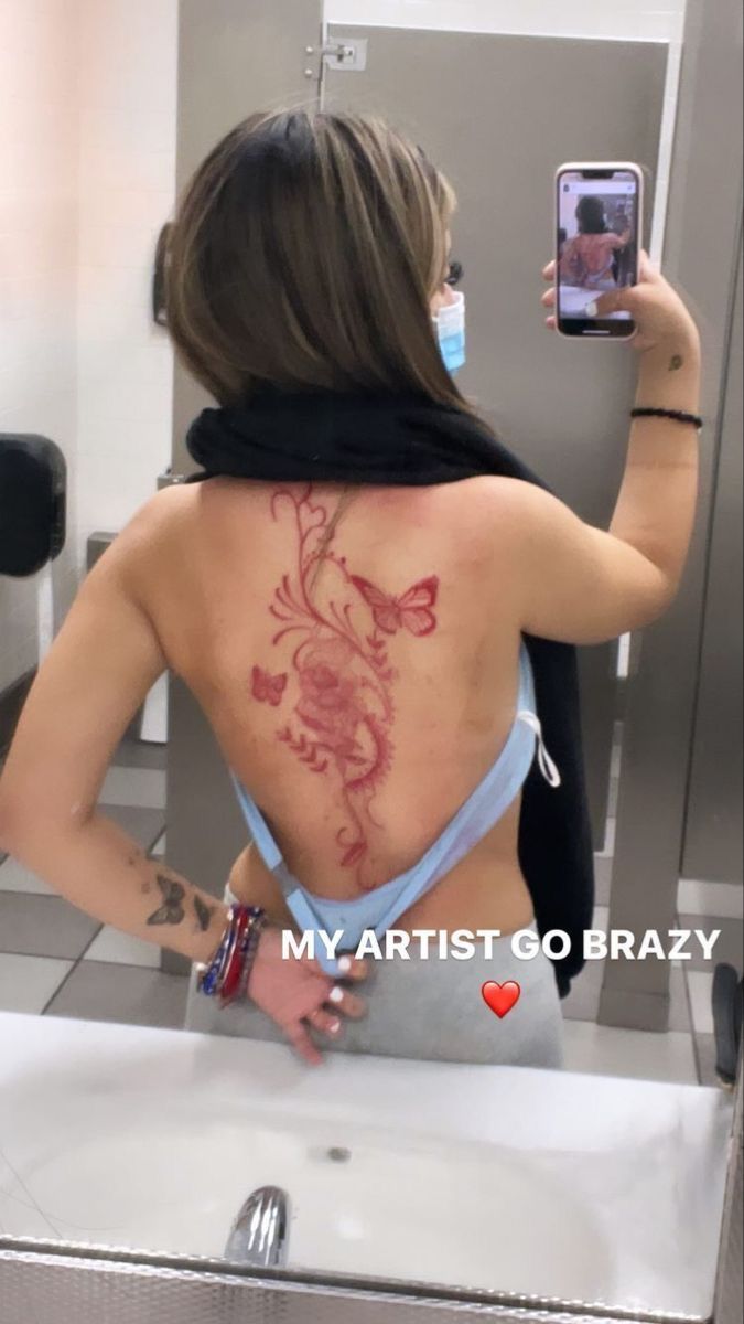 a woman taking a selfie in the mirror with her cell phone and tattoo on her back