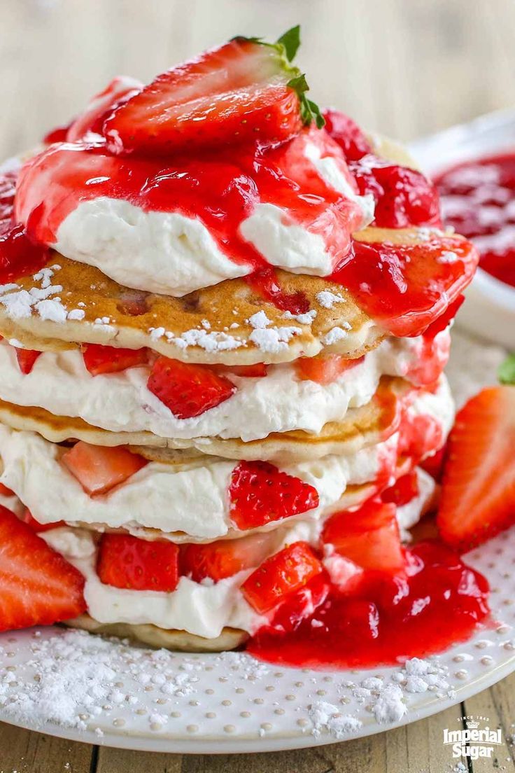 stack of strawberry shortcakes with whipped cream and strawberries on the plate next to it