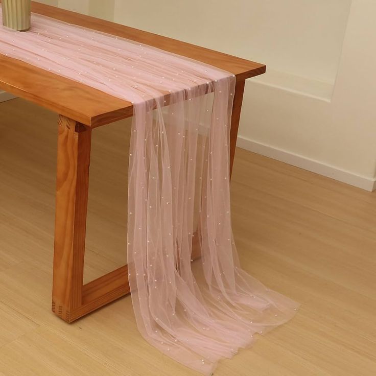 a wooden table with a pink cloth draped over it and a vase on the side