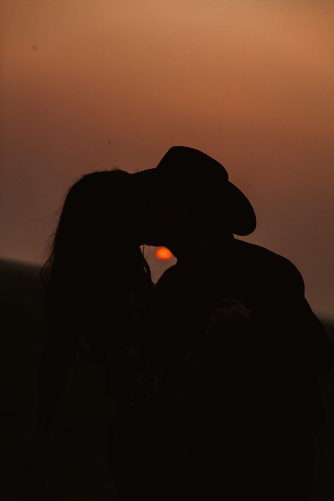 the silhouette of a man and woman kissing in front of an orange sky at sunset