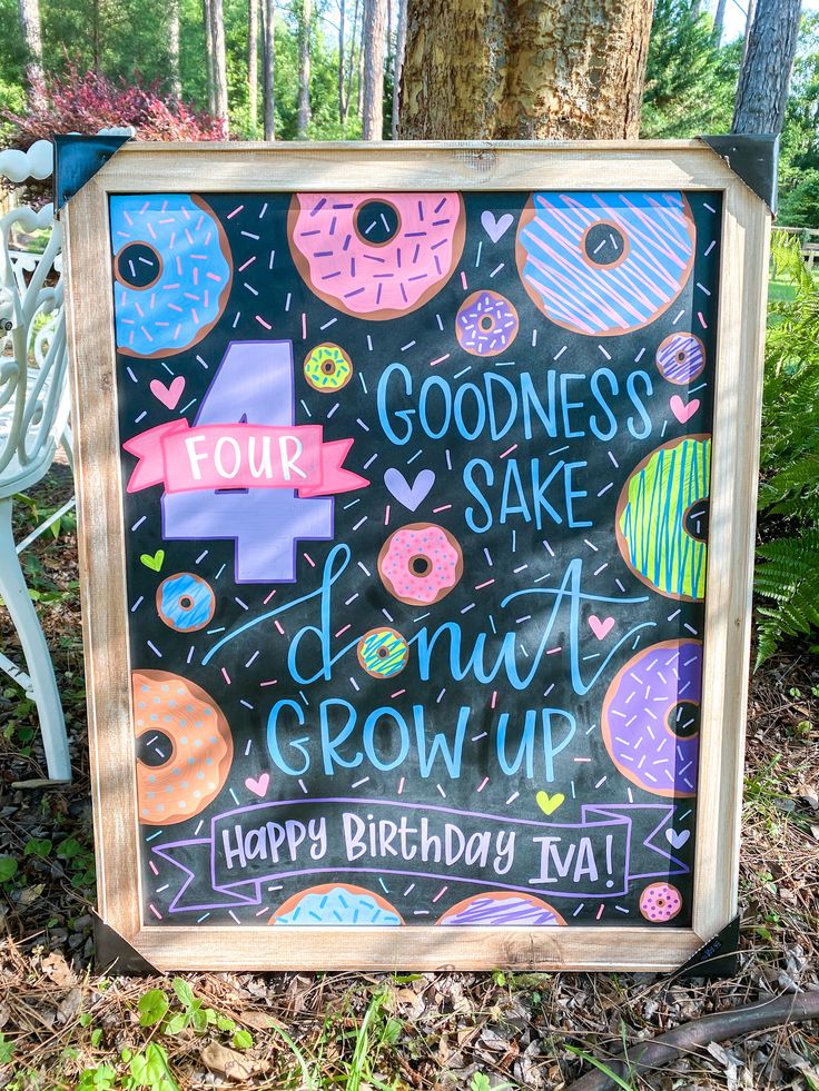 a chalkboard sign with donuts written on it in front of a bench and trees