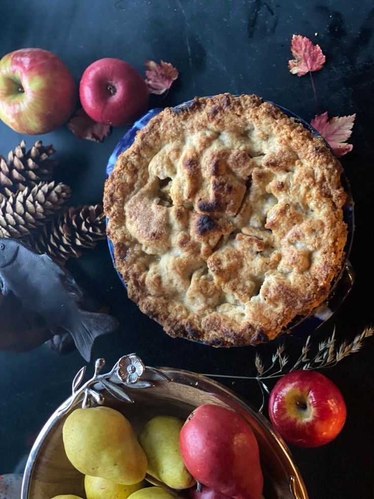 an apple pie next to some apples and pine cones