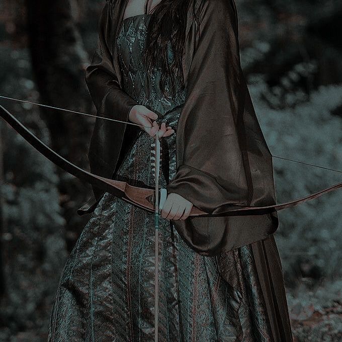 a woman dressed in medieval clothing holding a bow and arrow while standing in the woods