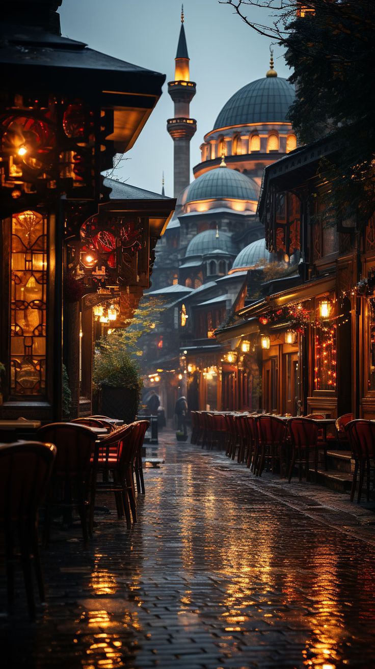 an empty street with tables and chairs on the side at night in front of a mosque