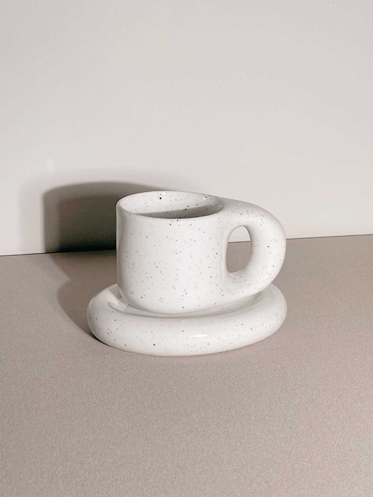 a white cup and saucer sitting on top of a counter next to a wall