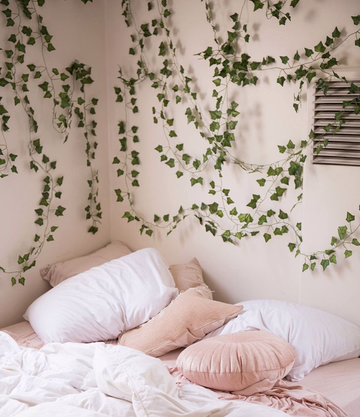 an unmade bed with white sheets and pillows covered in green ivy leaves on the wall