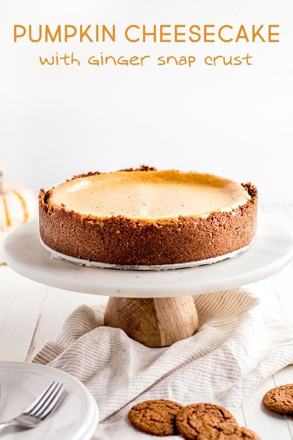 pumpkin cheesecake with ginger snap crust on a white cake platter next to cookies