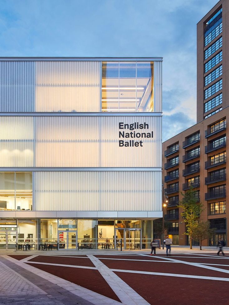 the exterior of an english national ballet building at dusk with people walking around and sitting on benches