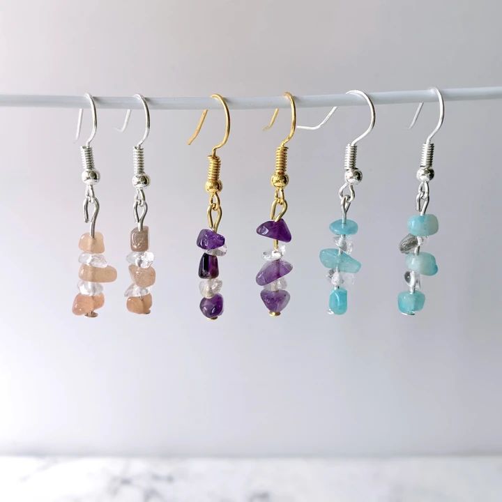 five pairs of earrings hanging from a line on a white background with marble counter top