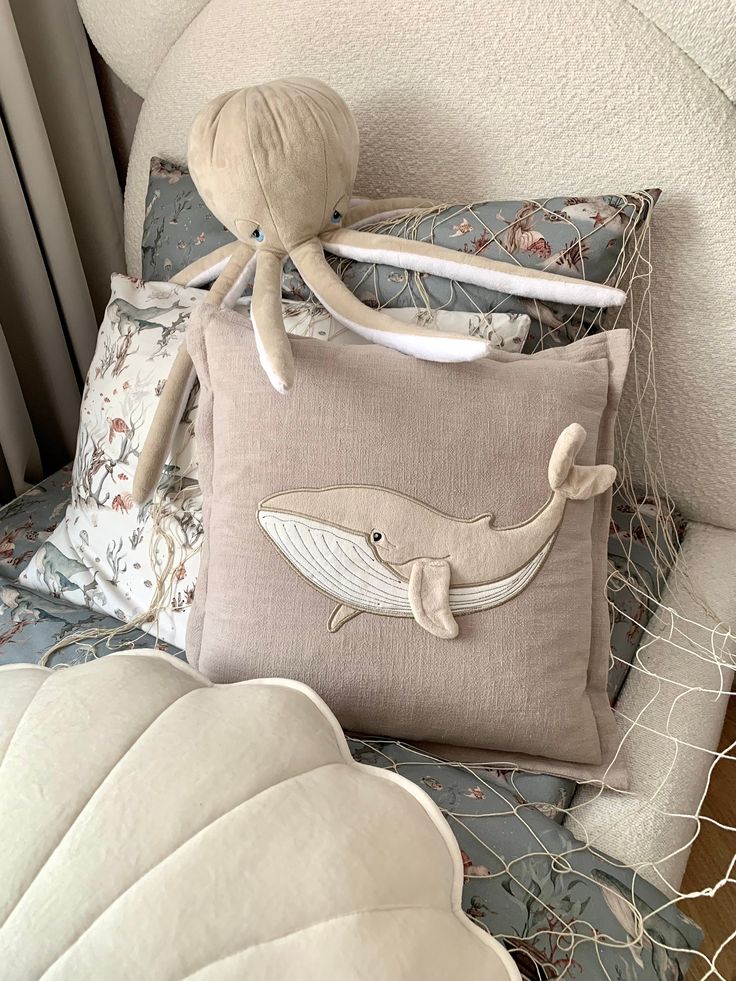 a stuffed whale sits on top of a pillow in the back of a chair with other pillows