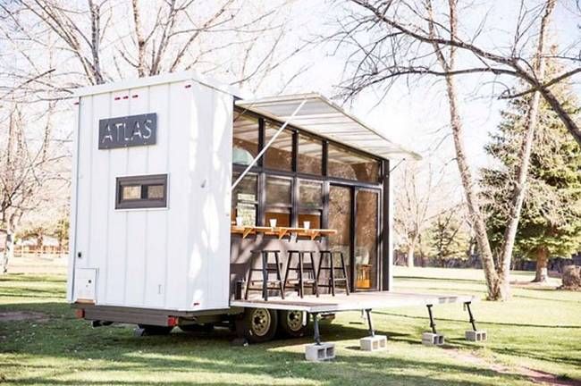 the tiny house is parked on the grass in front of some picnic tables and chairs