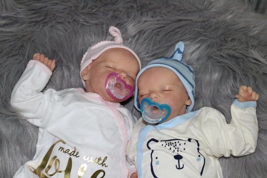 two baby dolls laying next to each other with pacifiers in their mouths on a furry surface