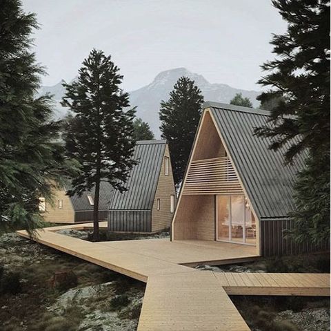 a wooden walkway leading to two small houses in the woods with mountains in the background