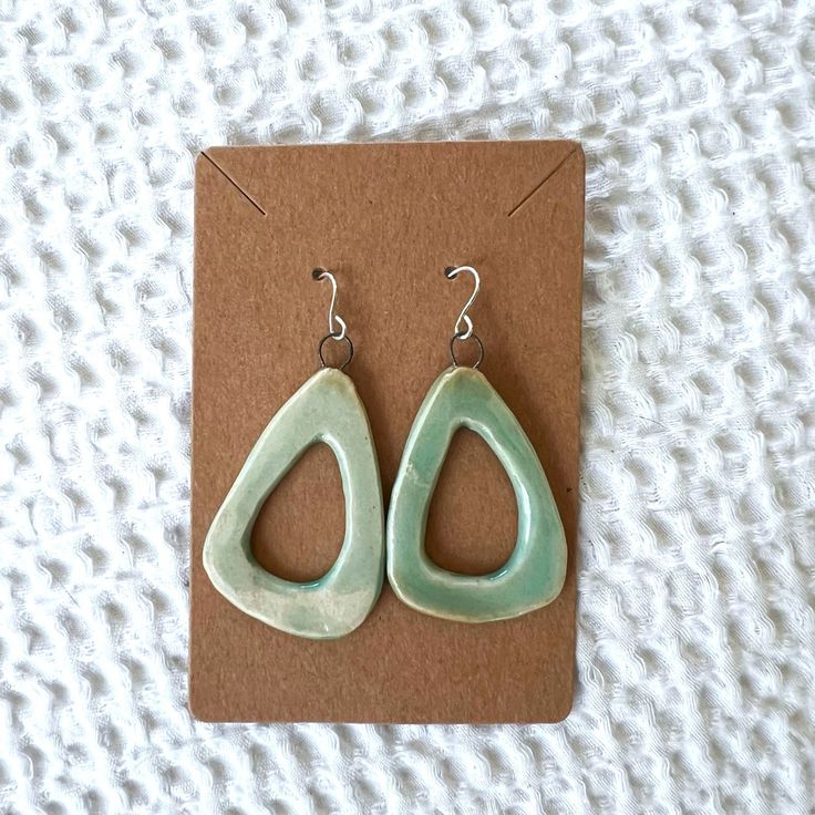 a pair of green earrings sitting on top of a piece of brown paper next to a card