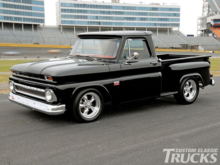 an old black pickup truck parked in front of a stadium