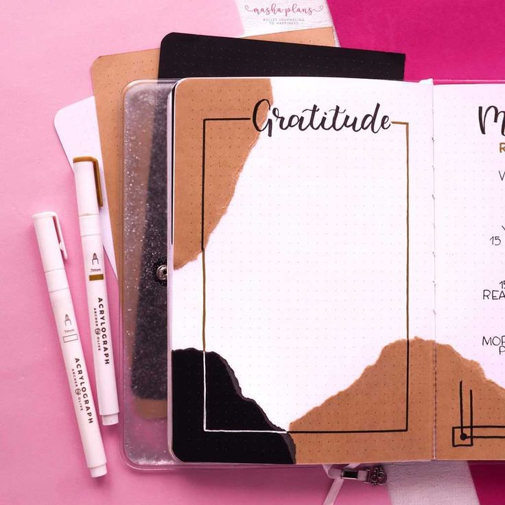 an open notebook sitting on top of a pink surface next to two pens and a clipboard