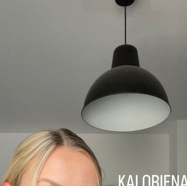 a woman is smiling and looking at the camera in front of a light hanging above her head