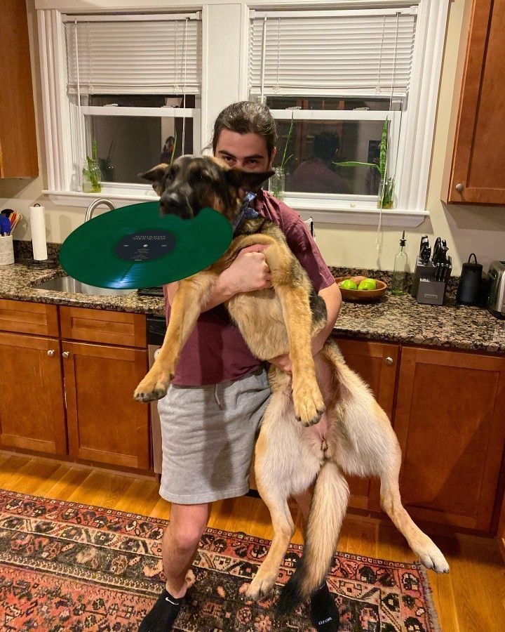 a man holding a dog in his arms while standing on top of a kitchen floor