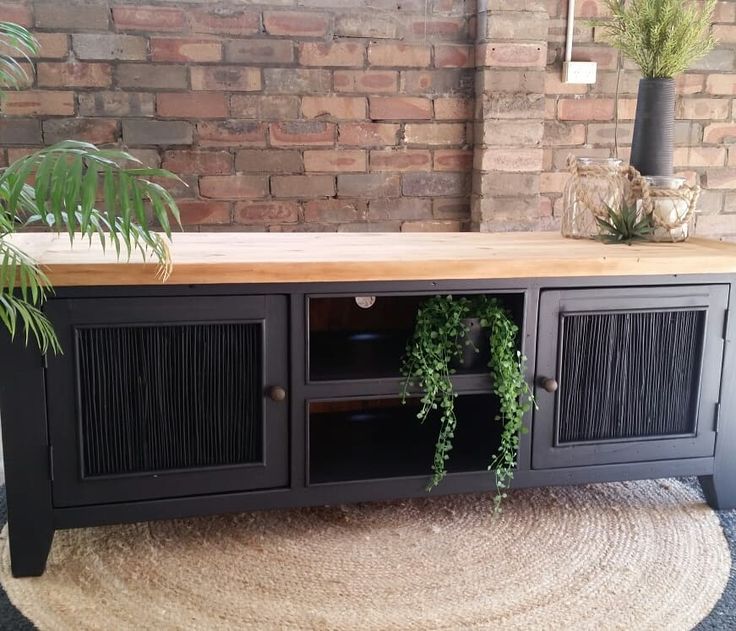 a black entertainment center with plants on top and a rug in the floor next to it