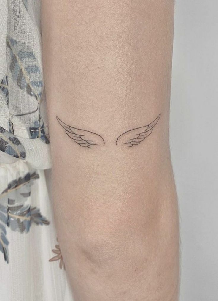 a woman's arm with an angel wing tattoo on the left side of her arm