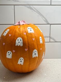 a pumpkin decorated with ghost faces and hearts is sitting on a counter in front of a white tile wall