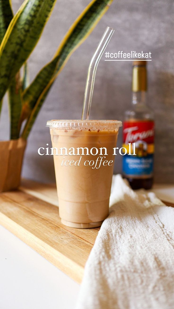 cinnamon roll iced coffee in a paper cup on a counter next to a potted plant