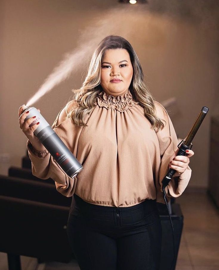 a woman is holding a hair dryer and spraying it with her hands while posing for the camera