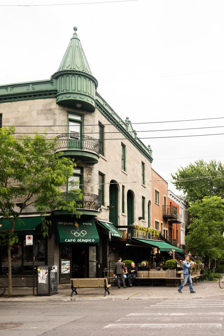 people walking down the street in front of an old building with green awnings