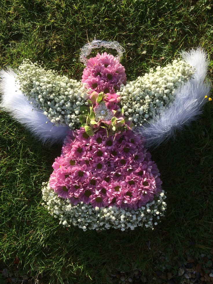 an angel made out of flowers and feathers on the ground with grass in the background