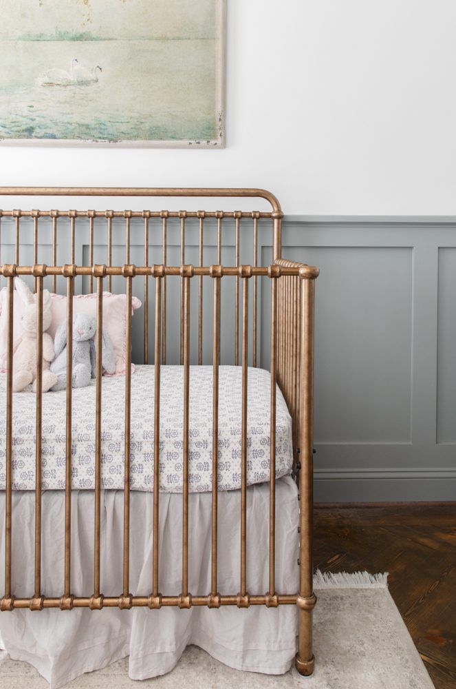 a gold crib in a white and gray nursery with a painting on the wall