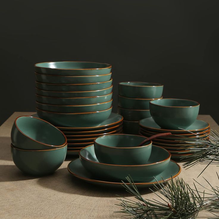 a table topped with lots of green plates and bowls next to a pine tree branch