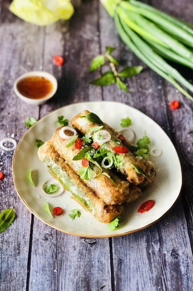 two pieces of food on a plate with sauces and green onions next to it