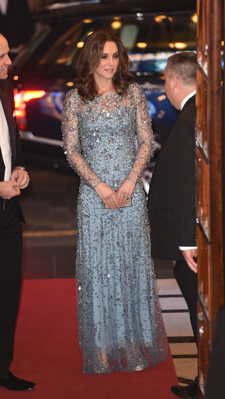 a woman in a long blue dress standing on a red carpet next to a man