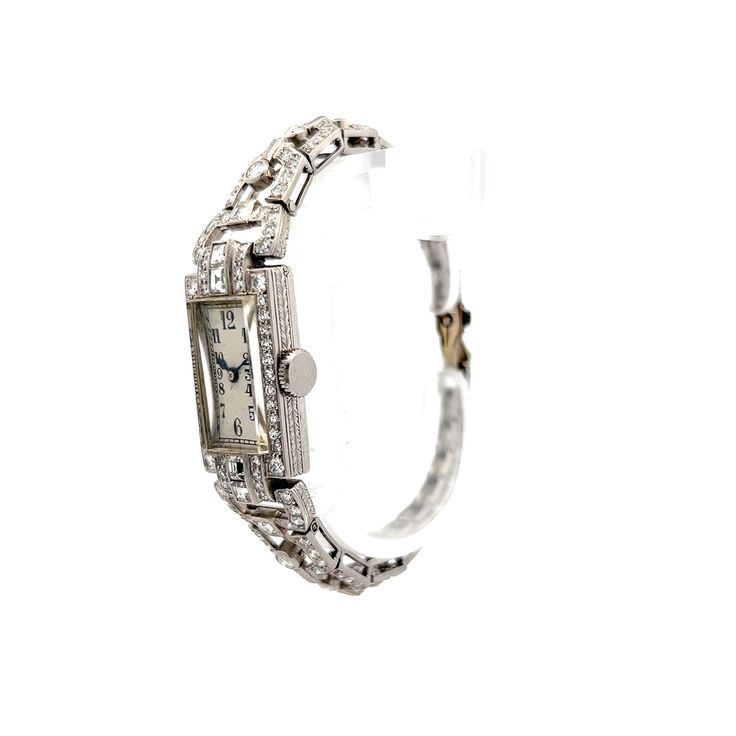 This antique Art Deco manual wind diamond watch, made from polished 14 karat white gold, features .60 carats of asscher cut diamonds with VS1 clarity and H color grade. Surrounding it are accent diamonds in various cuts, including old European, baguette, and single cuts, all bezel or channel set. These diamonds, ranging in size from 2.75 mm to 2.15 mm, contribute an additional .35 carats. The watch also showcases intricate milgrain detailing and engraving on the case, along with tapered links for added comfort. This vintage-inspired timepiece combines functionality with a rich sense of history. Classic Platinum Diamond Watch With Brilliant Cut, Classic Diamond White Watch With Brilliant Cut, Classic Wedding Jewelry And Watches With Diamond Hour Markers, Classic Diamond Jewelry With Brilliant Cut, Classic White Gold Jewelry With Brilliant Cut, Classic Diamond Accented Watch For Anniversary, Luxury Cubic Zirconia Watch For Anniversary, Art Deco Rectangular Watch With Diamond Hour Markers, Art Deco Rectangular Watch With Diamond Markers