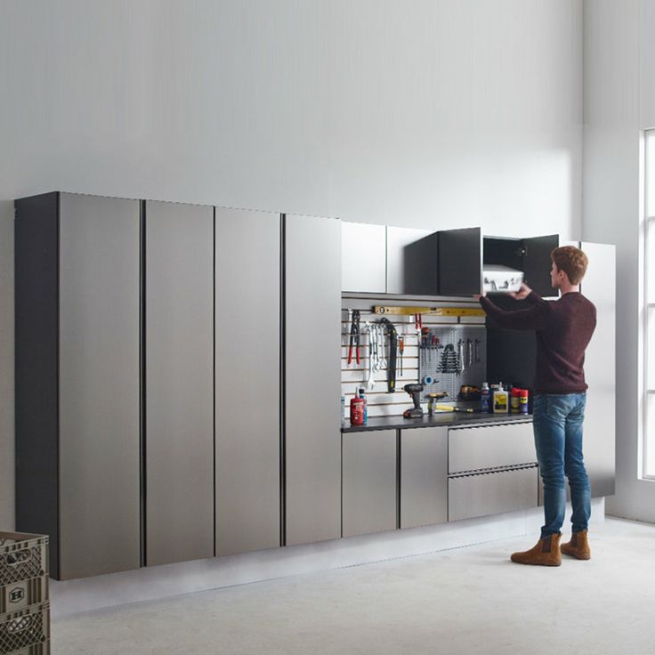 a man standing in the middle of a kitchen with stainless steel cabinets and appliances behind him