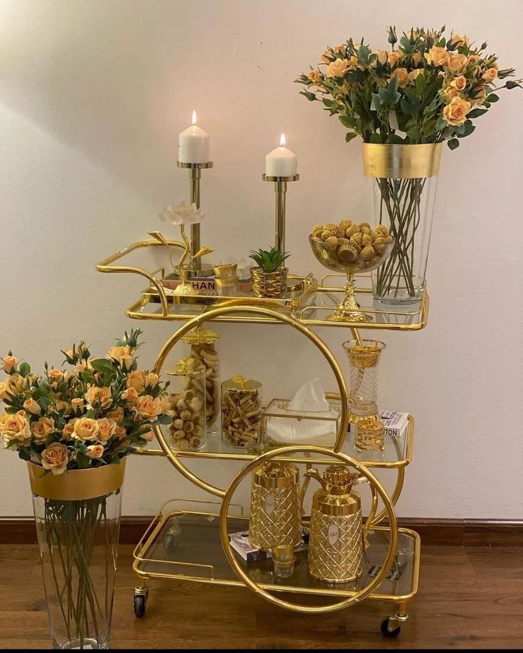 a gold bar cart filled with vases and flowers on top of a hard wood floor