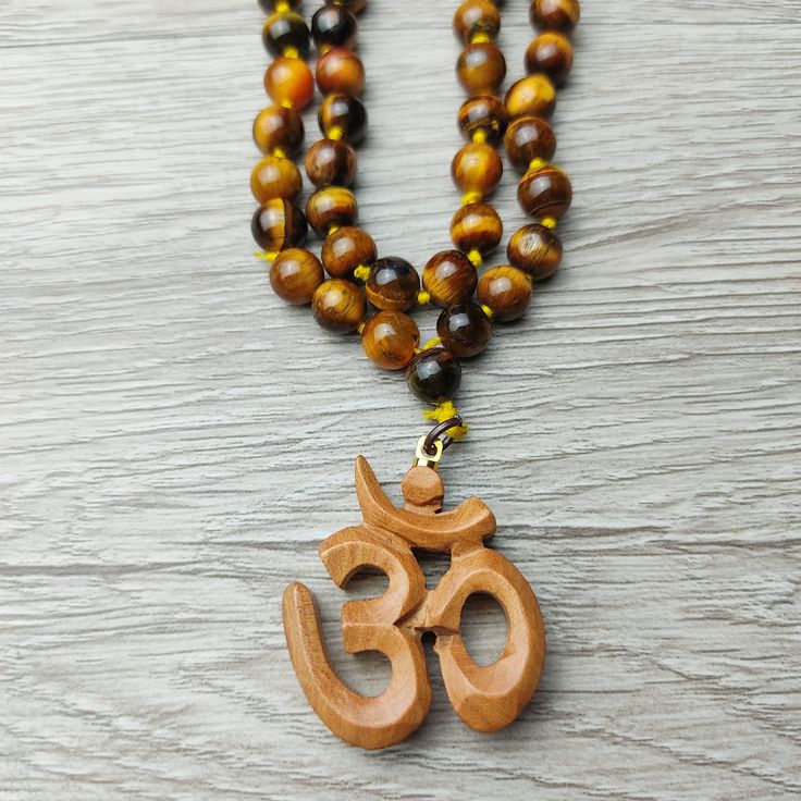 37" Unique Handcrafted Top Quality Tiger Eye Regal Beaded Knotted Necklace with Sandalwood Om Carved Scared Symbol. Sacred Amulet, Protection and Blessing Jewelry Gift. Handcrafted, Comes with A Velvet Pouch. ✥ Mala Necklace: 37" Long - 8mm beads ❀❀❀ Please look closely at photos as part of item description, the product in the images is as the one you will receive and is sold "as is". Please review the description and images prior to purchasing to ensure this item meets your satisfaction. We wel Brown Beaded Necklaces For Meditation And Festivals, Brown 8mm Beads Mala For Festival, Brown Beaded Mala For Festivals, Brown Mala With 8mm Beads For Festival, Brown Wooden Beads For Festivals, Festival Brown Beaded Mala, Bohemian Brown Mala For Festivals, Brown Necklace With 108 Beads For Festivals, Knotted Necklace