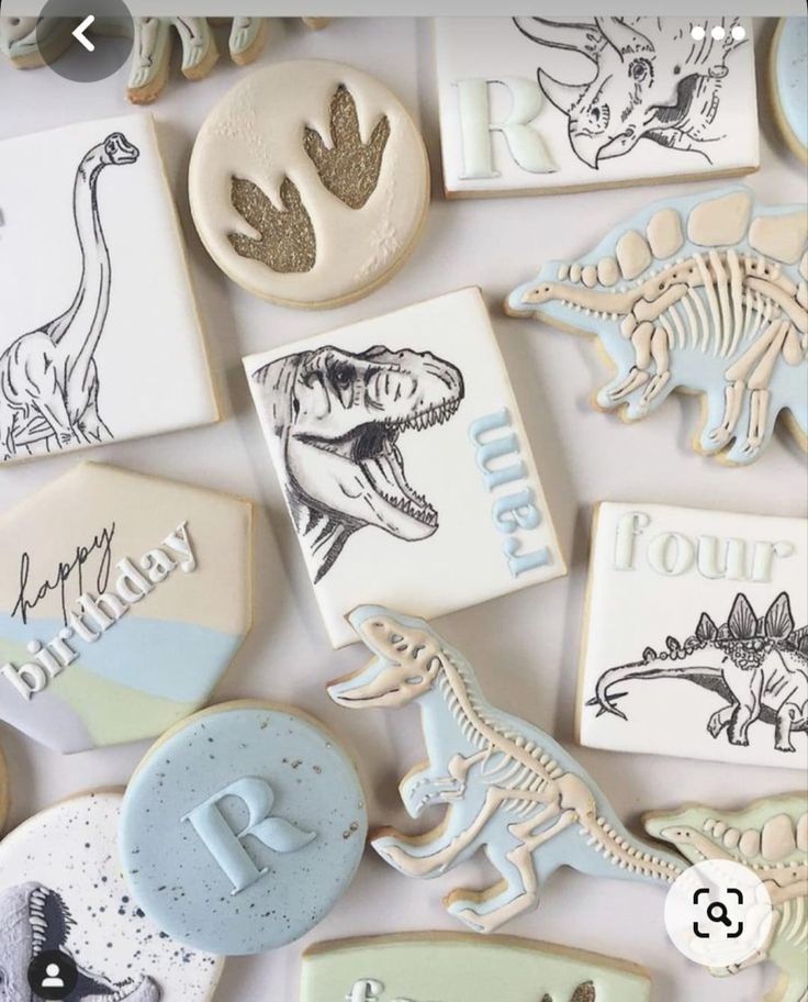 cookies decorated with dinosaur and typosauruss are displayed on a white tablecloth