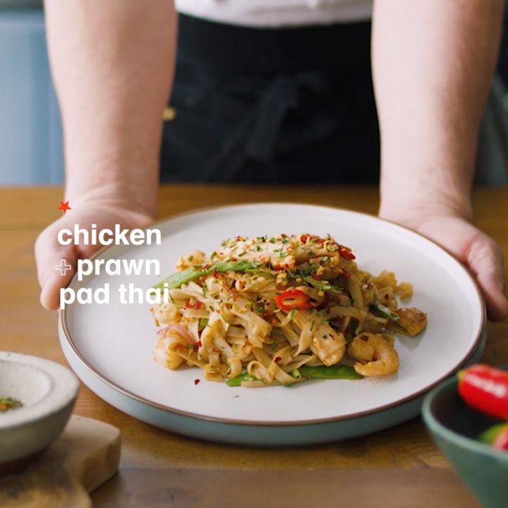 a person holding a white plate with food on it that reads chicken prawn pad thai