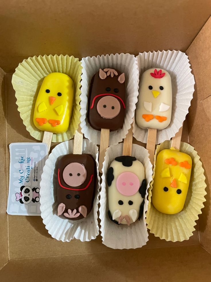 there are many desserts in the box on the table and one is decorated with farm animals