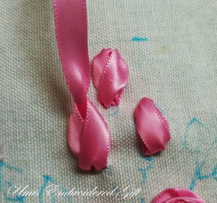 three pieces of pink satin ribbon sitting on top of a piece of fabric