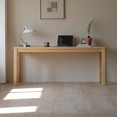 a wooden table with a laptop on it in front of a wall mounted clock and potted plant