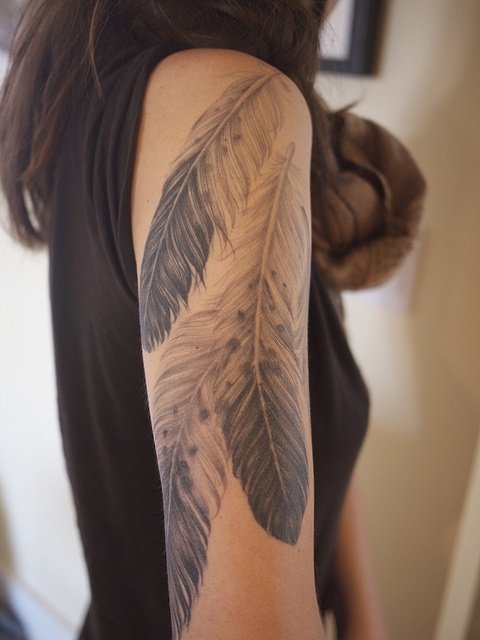 a woman with a tattoo on her arm has a feather design on it's arm